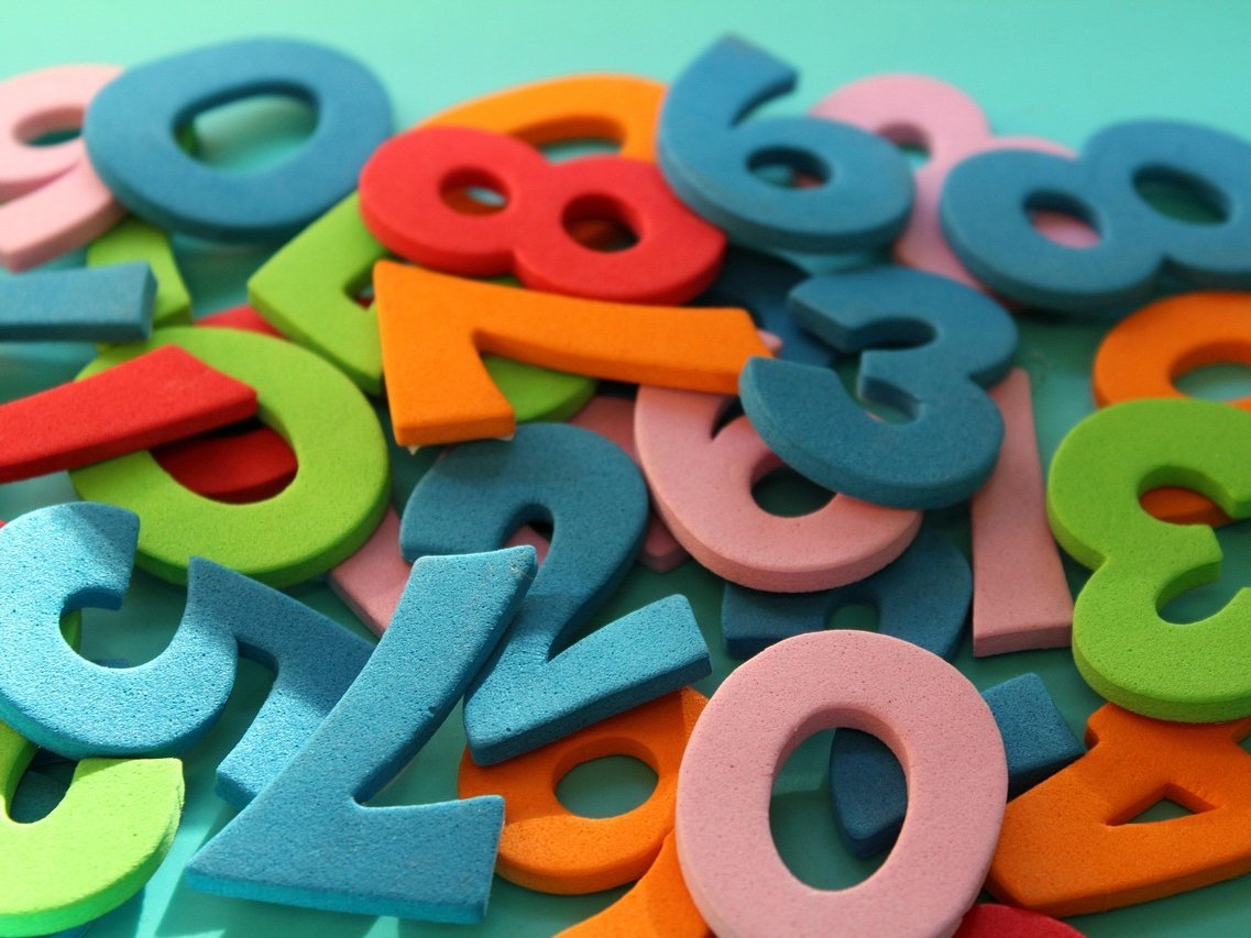 Bunt gemischte Zahlenwürfel mit Ziffern in verschiedenen Farben und Größen, verstreut auf einem grünen Hintergrund.