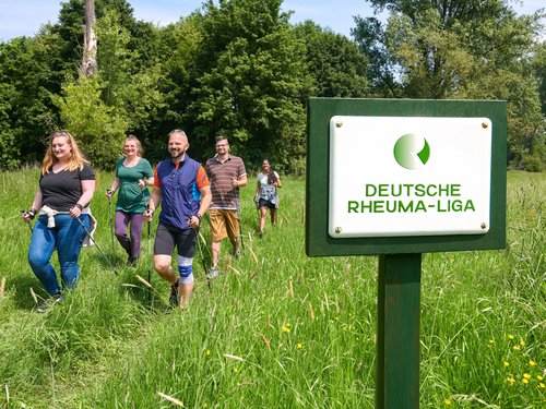 Gruppe von Menschen beim Nordic Walken, im Vordergrund Schild mit der Aufschrift "Deutsche Rheumaliga Bundesverband"