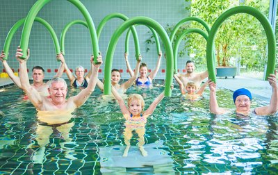 Mehrere Menschen mit Poolnudeln im Schwimmbad